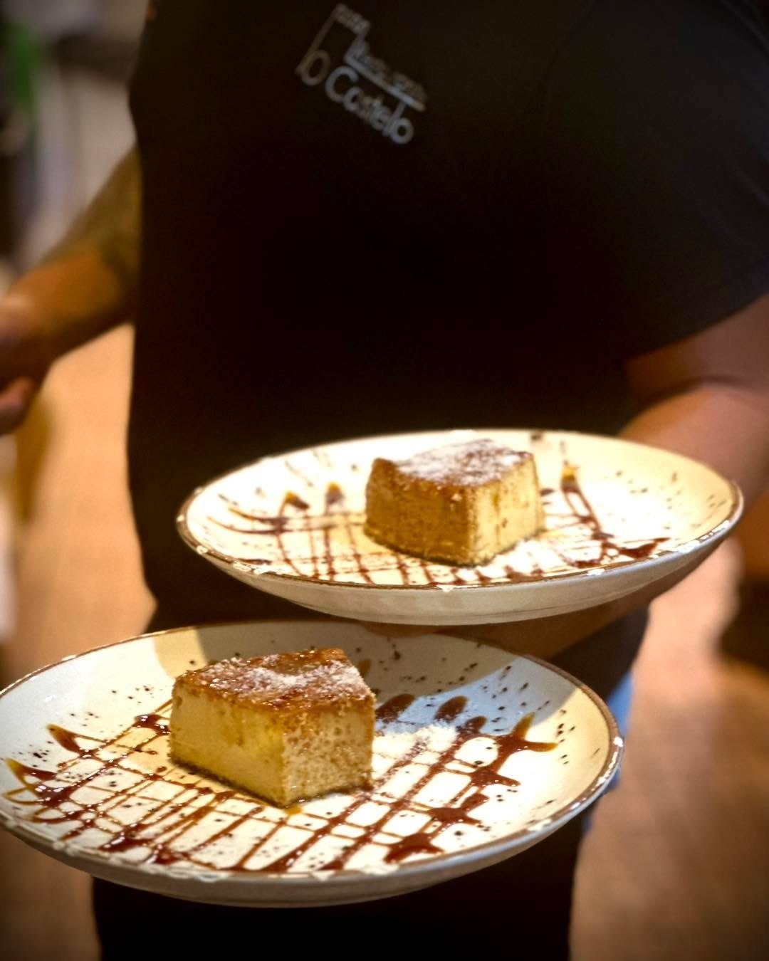 Duas fatias de pudim em pratos brancos com fios de caramelo, levadas à mesa